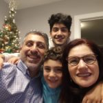 Family of four, father, mother and their two sons smiling in front of decorated Christmas tree